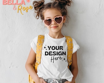 May include: A young person wearing a white t-shirt with the text "YOUR DESIGN Here" in black, paired with light blue jeans and a yellow backpack. They are wearing pink heart-shaped sunglasses. The background is a light gray wall.