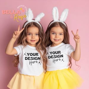 Op de afbeelding: Twee jonge meisjes dragen witte T-shirts met de tekst "YOUR DESIGN Here" erop gedrukt. Ze dragen konijnenoren-hoofdbanden en glimlachen naar de camera. De meisjes staan voor een roze achtergrond.