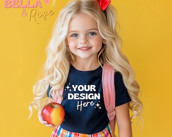 May include: A young girl with long blonde hair and a red bow, wearing a navy blue t-shirt with the text "YOUR DESIGN Here". She is holding an apple and wearing a pink backpack, with a colorful plaid skirt. The background is yellow.