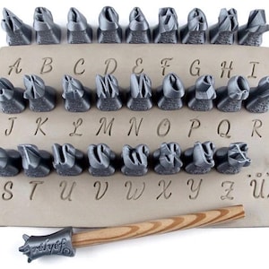 May include: A set of metal letter stamps arranged on a tan leather surface, with a wooden handled mallet. The letters A through Z are displayed, along with a few punctuation marks. The word "relief" is stamped on the mallet.