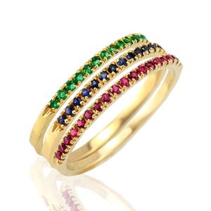 Könnte beinhalten: Drei goldene Ringe mit einer Reihe von Edelsteinen. Der obere Ring hat grüne Edelsteine, der mittlere Ring hat blaue Edelsteine und der untere Ring hat rote Edelsteine.