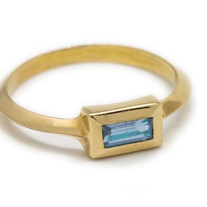 May include: A gold ring with a light blue rectangular gemstone set in a gold bezel.