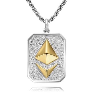 May include: Silver-tone pendant necklace featuring a rectangular pendant with a textured background and a gold-colored Ethereum symbol. The chain is a silver rope style. The pendant is approximately 1.5 inches long.
