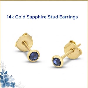 May include: Two gold stud earrings with round, dark blue sapphires. The earrings are set in a bezel setting and have a post and butterfly backing. The text "14k Gold Sapphire Stud Earrings" is at the top.