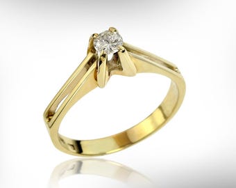 May include: A gold engagement ring with a single, round-cut diamond. The ring features a classic design with a split shank and a four-prong setting to secure the gemstone. The ring is made of yellow gold.