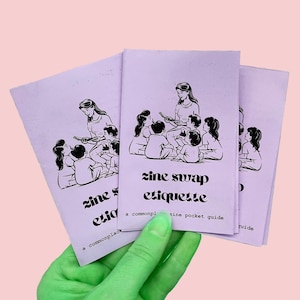 Puede incluir: Tres fanzines de color lavanda se sostienen en una mano. Cada fanzine presenta una ilustración en blanco y negro de una mujer leyendo a un grupo de niños. El texto "zine swap etiquette" está impreso en la portada, junto con la frase "a commonplace pocket guide."