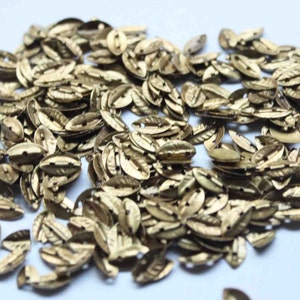 Puede incluir: Un montón grande de adornos de metal en forma de hoja de color dorado. Los adornos son pequeños y tienen una superficie ligeramente texturizada.