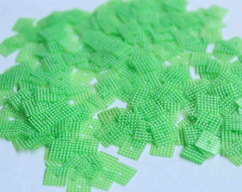 Op de afbeelding: Een stapel kleine, groene, vierkante pailletten met een textuur.
