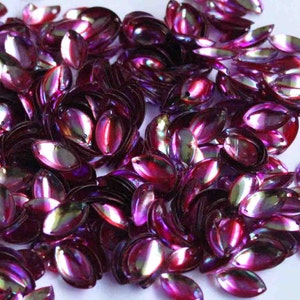 Puede incluir: Un montón grande de lentejuelas ovaladas iridiscentes de color púrpura y rosa. Las lentejuelas tienen un brillo metálico y son perfectas para manualidades y decoración.