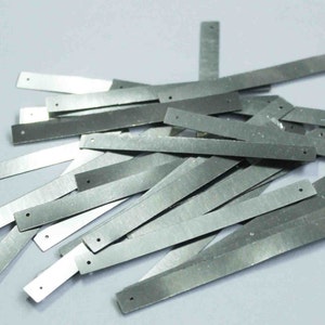May include: A pile of silver metal strips with holes punched in them. The strips are about 1 inch wide and 4 inches long.