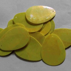 May include: A pile of yellow, oval-shaped craft supplies with small holes at the top. The supplies have a slightly textured surface and a pale yellow color. They are likely used for jewelry making or other crafts.