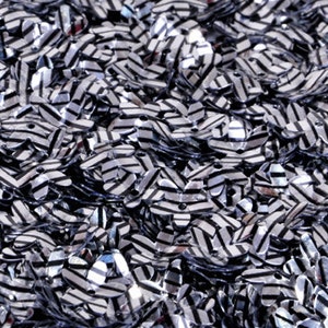 Peut inclure: Un grand tas de paillettes en forme de fleur rayées argent et noir. Les paillettes sont brillantes et ont une finition métallisée.