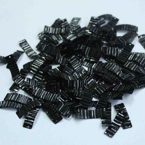 Puede incluir: Un montón de lentejuelas metálicas negras con una superficie ondulada y texturizada. Las lentejuelas tienen forma de pequeños rectángulos con esquinas redondeadas.