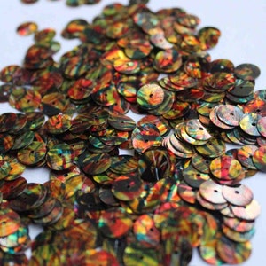 May include: A large pile of round, iridescent sequins with a colorful abstract pattern. The sequins are mostly black, red, orange, and green.