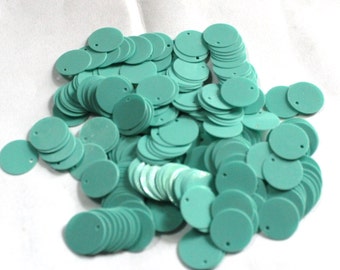 May include: A pile of teal-colored, round sequins with a small hole at the top. These flat, disc-shaped sequins are scattered across a white surface. They are ideal for embellishing clothing, accessories, or craft projects.