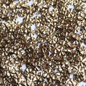 May include: A close-up of a pile of gold-colored sequins. The sequins are round and have a slightly raised center.