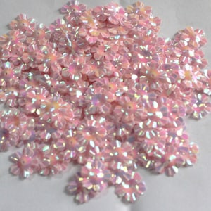 Puede incluir: Un montón de lentejuelas de color rosa iridiscente en forma de flor. Las lentejuelas tienen un centro ligeramente elevado y un borde festoneado.