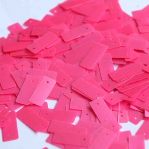 Könnte beinhalten: Ein großer Haufen von rechteckigen Pailletten in leuchtendem Pink. Die Pailletten haben oben ein Loch zum Nähen.