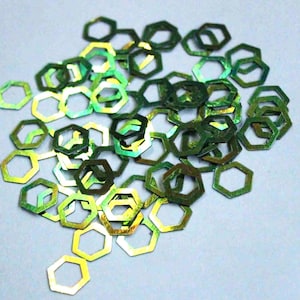 May include: A pile of green and gold iridescent hexagonal confetti.