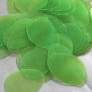 May include: A pile of lime green oval-shaped sequins. The sequins are translucent and have a slight shimmer.