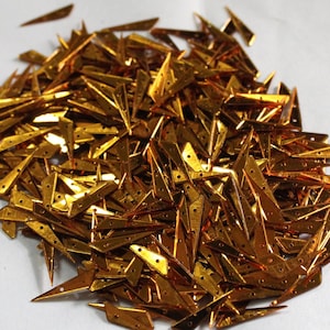May include: A large pile of gold-colored metallic sequins shaped like arrowheads.