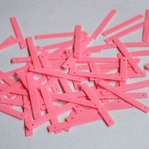 May include: A pile of pink plastic craft supplies, resembling small strips with holes, for making jewellery or other crafts.
