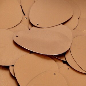 May include: A pile of oval-shaped sequins in a metallic gold colour. The sequins have a hole in the centre for sewing.