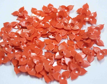 Op de afbeelding: Een grote hoeveelheid kleine, oranje, plastic bloemvormige versieringen. De versieringen hebben vijf bloemblaadjes en een klein gaatje in het midden.
