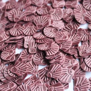 Puede incluir: Una gran pila de botones de cerámica rosa con un diseño de ojo decorativo. Los botones son todos de la misma forma y tamaño, y están dispuestos en un patrón aleatorio.