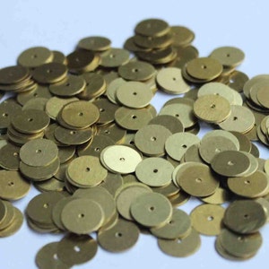 May include: A large pile of gold-colored metal discs with a small hole in the center. The discs are arranged in a random pattern.