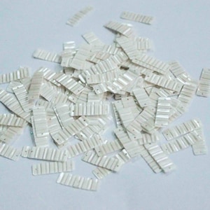 May include: A pile of white iridescent sequins with a slightly rippled texture. The sequins are rectangular in shape.