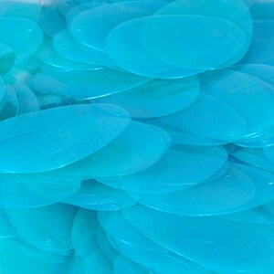 May include: A pile of turquoise blue oval-shaped sequins. The sequins are translucent and have a slight shimmer.