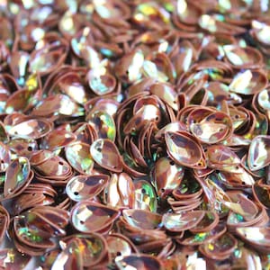 May include: A large pile of iridescent, pearlescent, teardrop-shaped sequins in a copper colour.