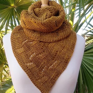 May include: A triangular knitted scarf in a warm brown color with a lacy pattern. The scarf is draped over a white mannequin.