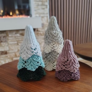 Könnte beinhalten: Drei gehäkelte Weihnachtsbäume in verschiedenen Größen und Farben. Der größte Baum ist ein Farbverlauf aus Grün, Türkis und Hellblau. Der mittlere Baum ist weiß und grau. Der kleinste Baum ist lila. Alle Bäume haben ein geschichtetes Design.