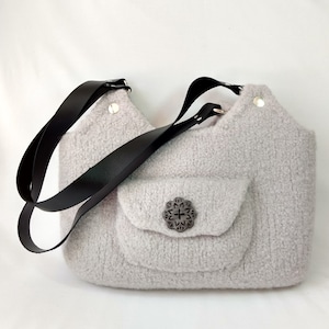 May include: A light gray fuzzy shoulder bag with a black leather strap and a decorative button. The bag has a small pocket on the front.