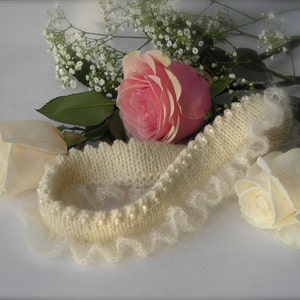 May include: A white knitted headband with a pearl trim and a delicate lace edge. The headband is surrounded by white and pink roses.