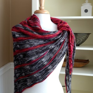 Könnte beinhalten: Ein gestrickter Schal in Grau und Rot mit einem Lochmuster. Der Schal ist über eine weiße Schaufensterpuppe gelegt.