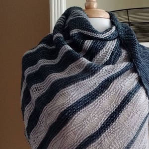 Könnte beinhalten: Ein handgestrickter Schal in Marineblau, Grau und Off-White. Der Schal hat diagonale Streifen und ein strukturiertes, offenes Webmuster. Das Kleidungsstück ist über eine Schaufensterpuppe drapiert, um seinen Fall und sein Muster zu zeigen.