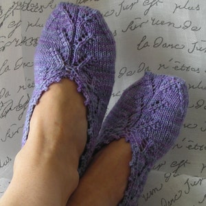 May include: A pair of purple and blue knitted slippers with a lacy design. The slippers are worn on a person's feet.