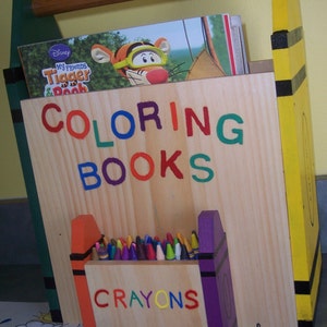 May include: A wooden storage box with a yellow and black striped side. The box is labeled "COLORING BOOKS" and has a smaller compartment labeled "CRAYONS". The box is filled with crayons and a coloring book featuring Tigger and Pooh.