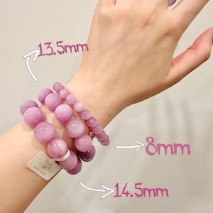 May include: Three bracelets with varying sizes of round, light purple beads. The largest beads are 14.5mm, the medium beads are 13.5mm, and the smallest beads are 8mm. A matching ring is on a hand.