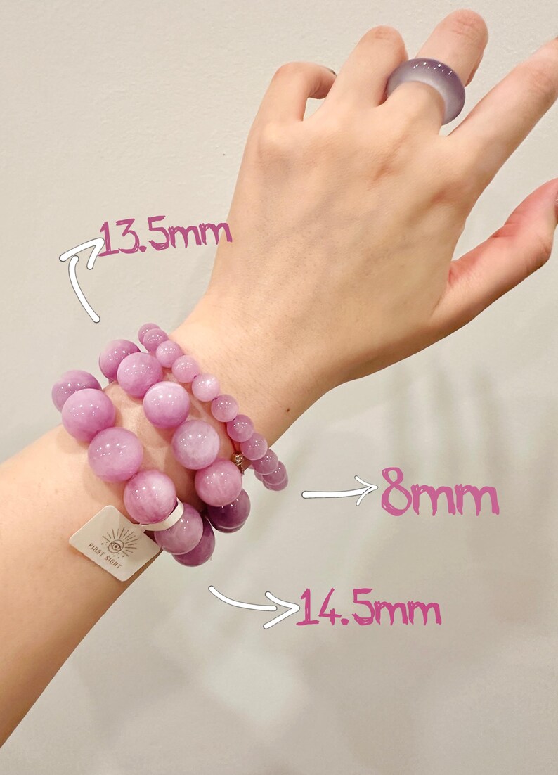 May include: Three bracelets with varying sizes of round, light purple beads. The largest beads are 14.5mm, the medium beads are 13.5mm, and the smallest beads are 8mm. A matching ring is on a hand.
