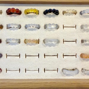 Peut inclure: Présentation de bagues en pierres précieuses dans un présentoir en bois. Les bagues présentent diverses couleurs, notamment transparent, rouge, jaune, noir et orange. Chaque bague est composée de plusieurs petites pierres arrondies.