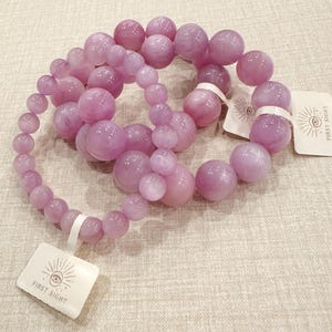 May include: A collection of light purple beaded necklaces with varying bead sizes. The beads have a glossy finish. Each necklace is attached to a white tag with the text "FIRST SIGHT" and an eye design.