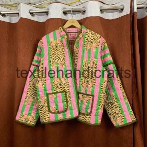 May include: A quilted jacket with a vibrant design. The jacket features vertical pink and green stripes, with tiger print panels. The jacket has two pockets and is lined with a contrasting fabric. The text "textilehandicrafts" is visible on the jacket.