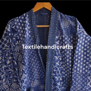 May include: A blue and white patterned kimono-style robe with a dark blue trim and the text "Textilehandicrafts". The robe is hanging on a wooden hanger against a black background. The pattern includes floral and geometric designs.