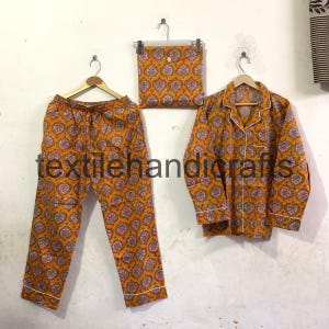 Può includere: Set pigiama arancione con motivo floreale rosa e bianco. Il set include pantaloni, camicia con bottoni e pochette abbinata. Il testo "textilehandicrafts" è visibile sui pantaloni.