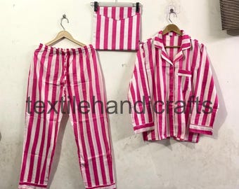 May include: A set of pink and white striped pajamas, including pants, a long-sleeved button-down shirt, and a matching pillowcase. The pajamas are hanging on wooden hangers against a neutral wall. The text "textilehandicrafts" is visible.