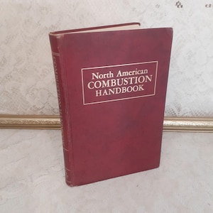 May include: A maroon hardcover book titled "North American Combustion Handbook" in a white rectangular box. The book is standing upright, with the title clearly visible. The book's spine has text running vertically.